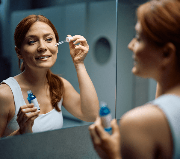 Woman applying skincare serum in mirror.
